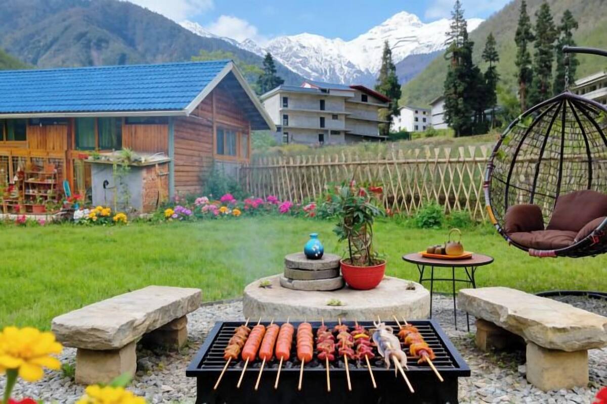 Eine Holzhütte mit blauem Dach, einem Hängestuhl und einem Grill mit Spießen.