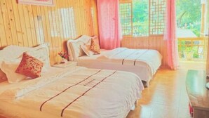 A wooden room with two beds, a small table, and a window with a view of greenery.