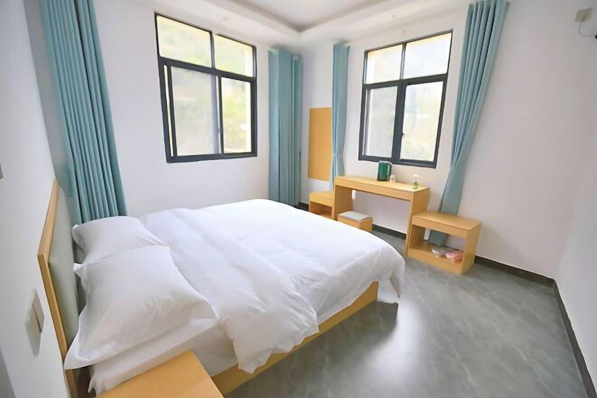 Ein Schlafzimmer mit Bett, Schreibtisch und Stuhl. Zwei Fenster mit Vorhängen.