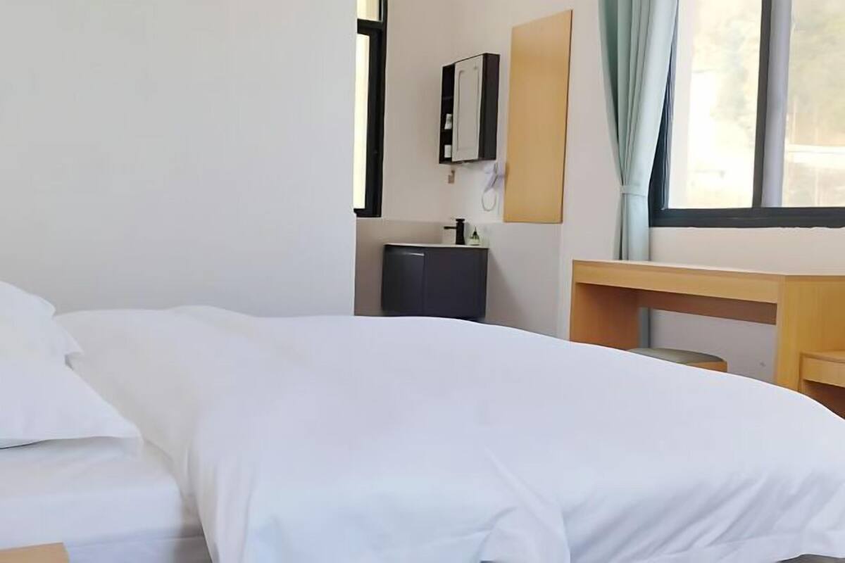 Ein Hotelzimmer mit Bett, Nachttisch, einem kleinen Schrank und einem Fenster mit Vorhängen.