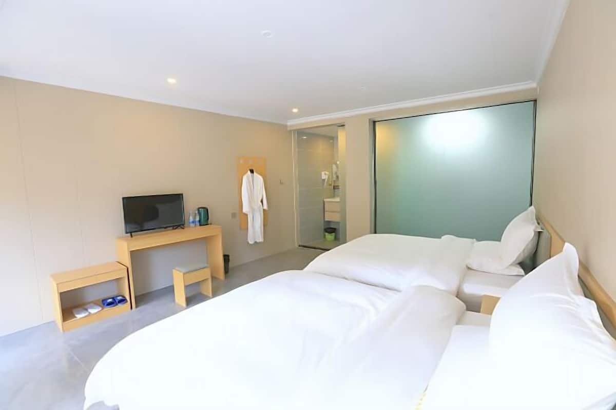 Habitación de hotel con cama, televisión, escritorio y baño visible a través de una puerta de vidrio.