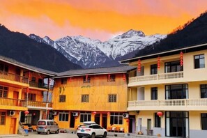 Un edificio con varios balcones, un coche estacionado en la parte delantera y montañas nevadas al fondo.