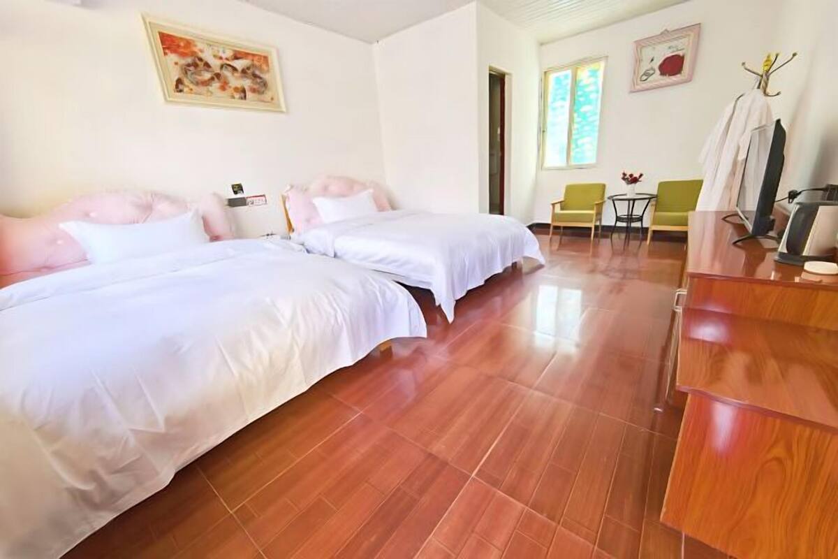 Ein Hotelzimmer mit zwei Betten, Holzboden, einem Schreibtisch, Stühlen und Bildern an den Wänden.