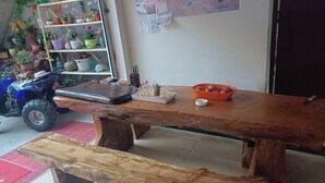 A rustic wooden table with a bench, surrounded by potted plants and a small orange bowl.