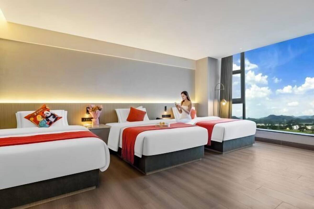 A hotel room with two beds, a large window, and a view of the cityscape.