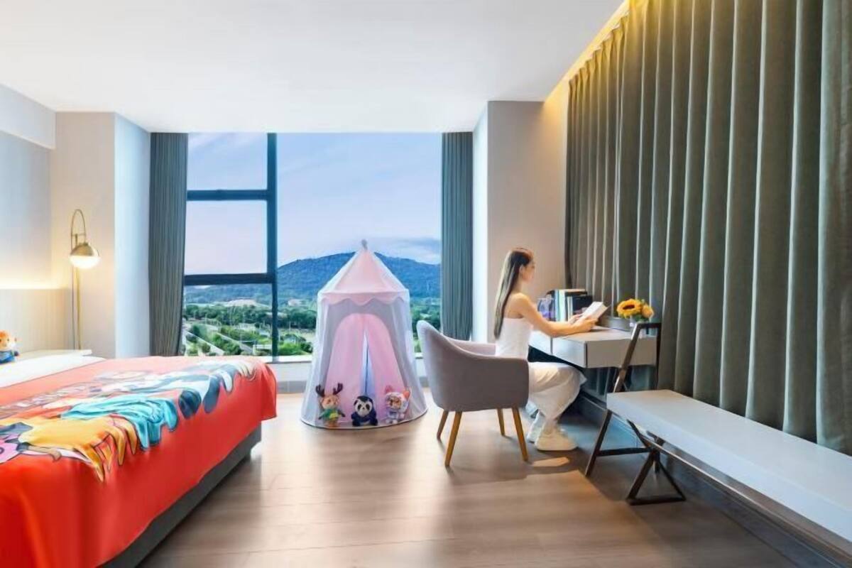 A modern hotel room with a bed, desk, chair, and a view of the landscape.