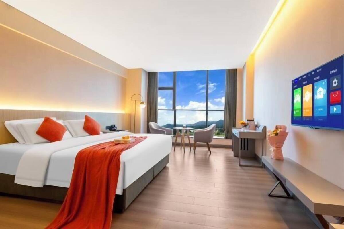 A modern hotel room with a large bed, a desk, and a TV on the wall.