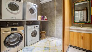 A laundry area with multiple washing machines, a small shelf with cleaning supplies, and a tiled floor. - Foshan Yuefeng High-altitude Garden Panorama Hotel (Jiujiangzhen Xinji Plaza) (Foshan)