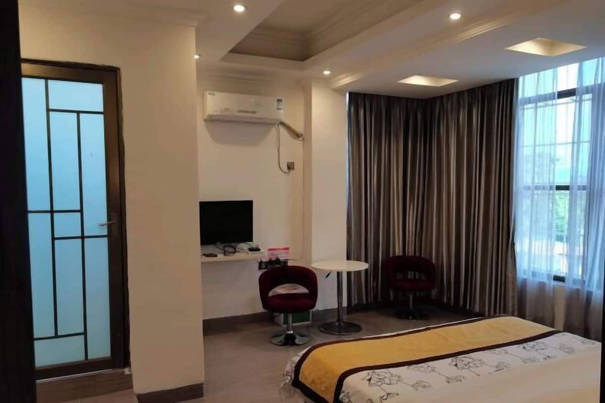 Ein Hotelzimmer mit einem Bett, einem Schreibtisch, zwei Stühlen, einem Fernseher und einem Fenster mit Vorhängen.
