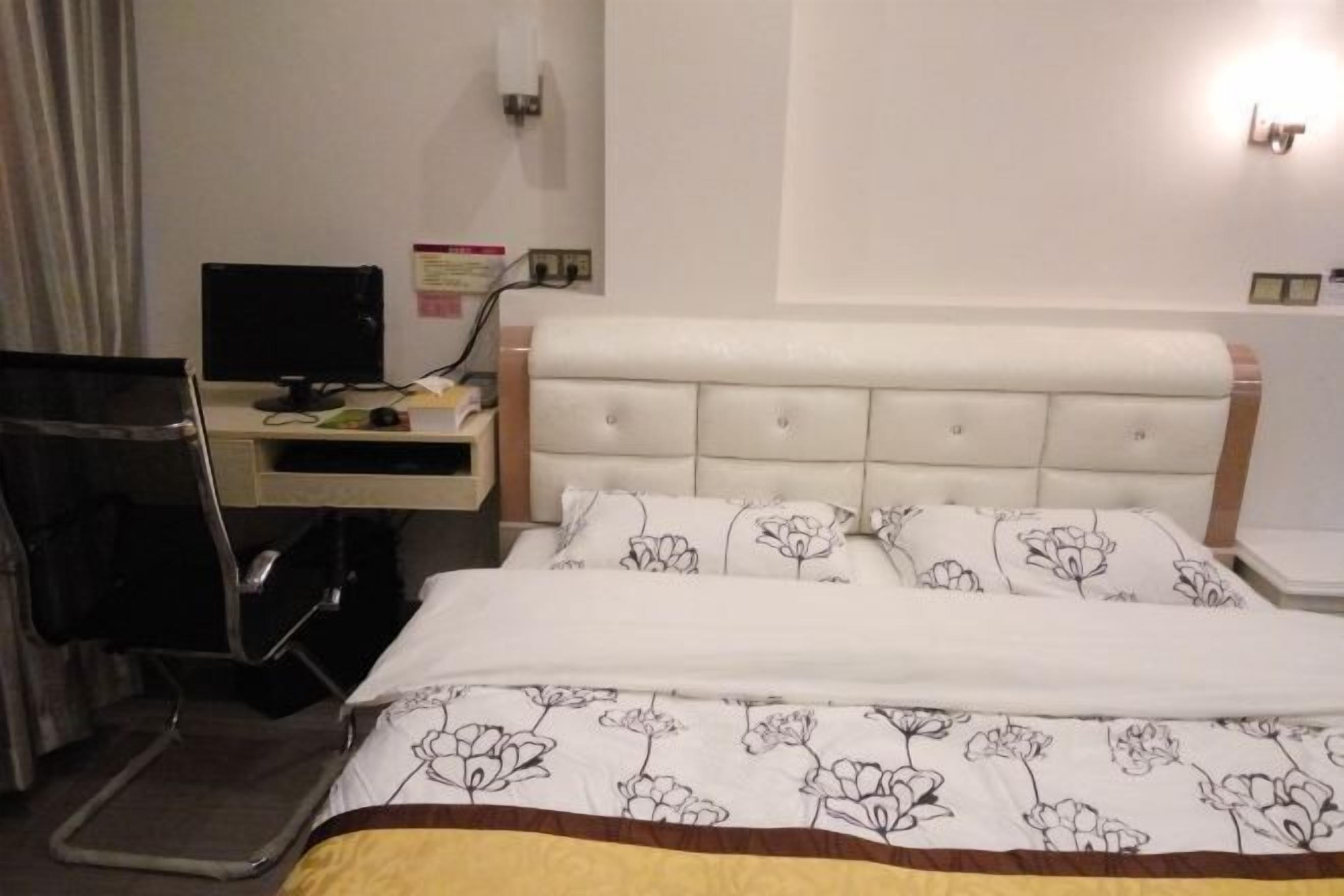 A hotel room with a bed, a desk with a computer, and a chair.