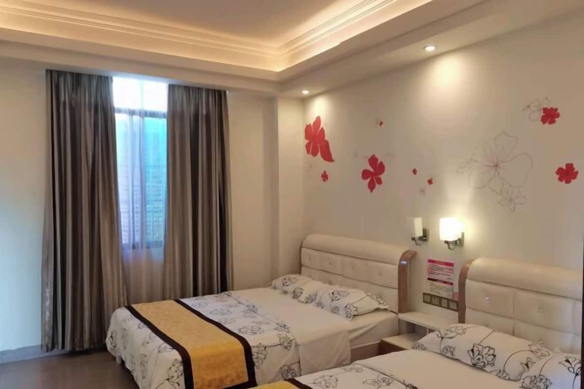 Ein Hotelzimmer mit zwei Betten, einem Fenster mit Vorhängen, einer Wand mit floralen Aufklebern und einem Nachttisch mit Lampe.