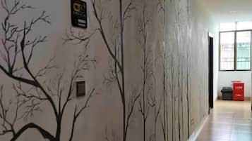 Un couloir orné d’une fresque murale représentant des arbres sans feuilles, d’un panneau de sécurité incendie et d’une poubelle.