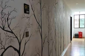 A hallway with a wall mural of bare trees, a fire safety sign, and a trash bin. - Nanxiong Huangkeng Town Minyi Tourism Accommodation (Nanxiong)