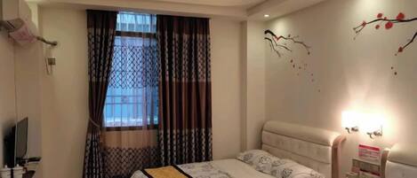 A hotel room with a bed, bedside table, and a window with curtains.