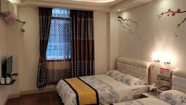 Ein Hotelzimmer mit zwei Betten, einem Fernseher, einem Nachttisch mit Lampe und einem Fenster mit Vorhängen.