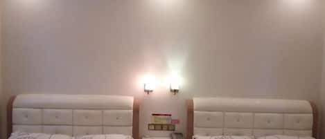 Una habitación de hotel con dos camas, cada una con una colcha de diseño floral, una mesita de noche con hervidor y teléfono, y una lámpara de pared.