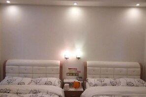 A hotel room with two beds, each with a floral-patterned duvet, a bedside table with a kettle and a phone, and a wall-mounted light fixture. - Nanxiong Huangkeng Town Minyi Tourism Accommodation (Nanxiong)