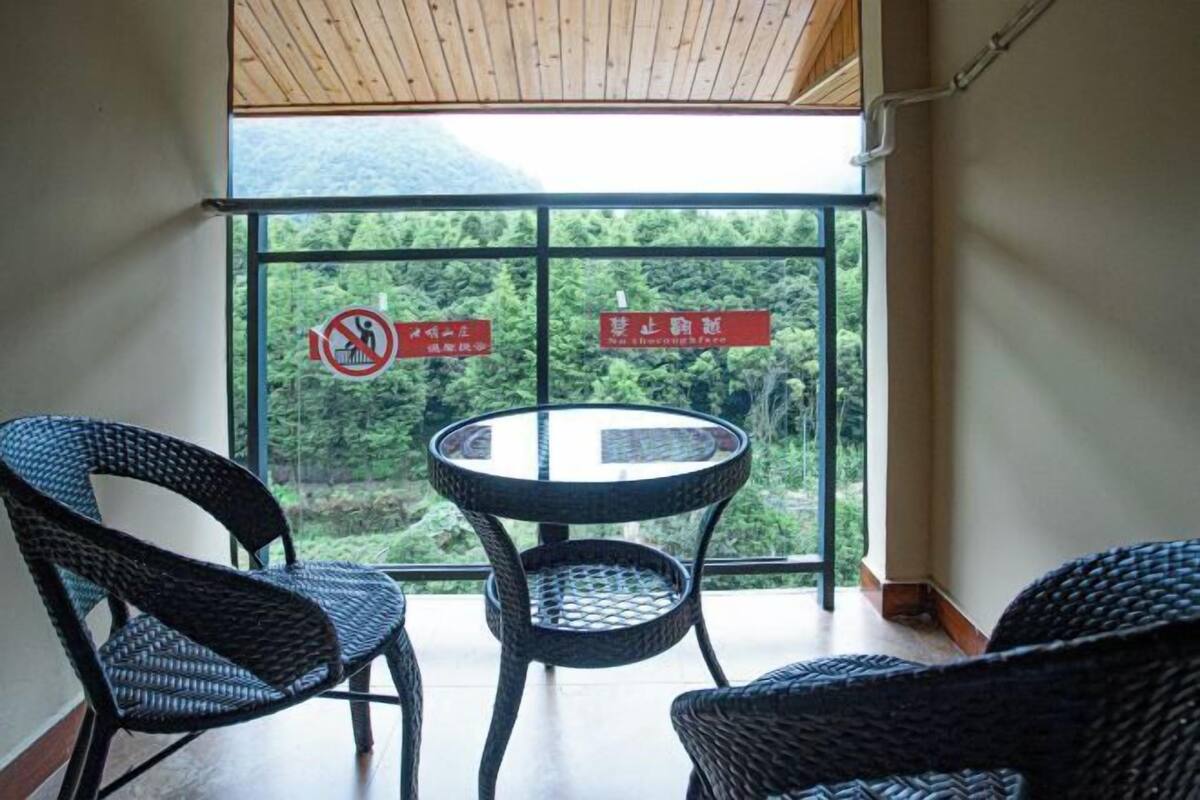 Uma varanda com cadeiras de vime e uma mesa, com vista para uma área arborizada.
