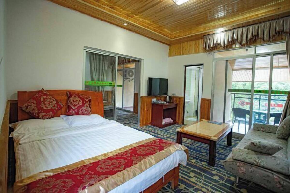 Quarto de hotel com uma cama grande, cabeceira de madeira, televisão, mesa pequena e um sofá.