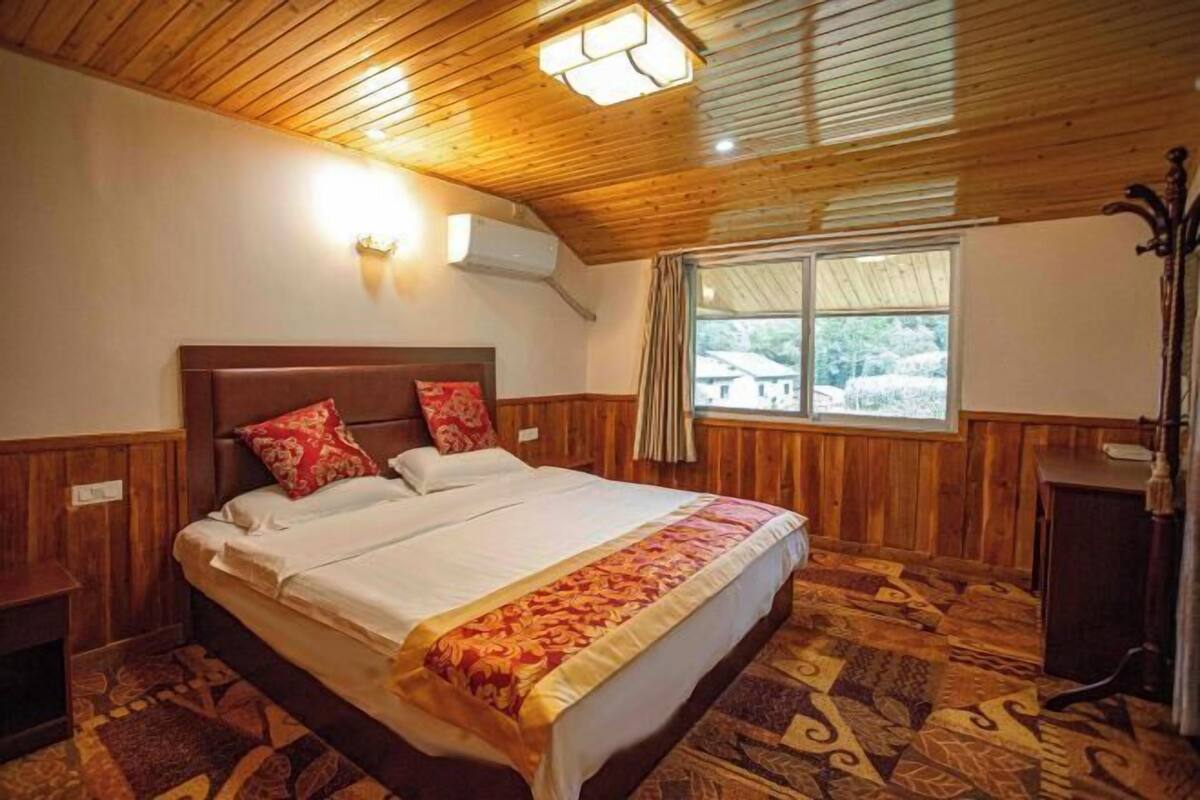 Quarto com teto de madeira, cama com colcha estampada, janela com cortinas e mesa de cabeceira.