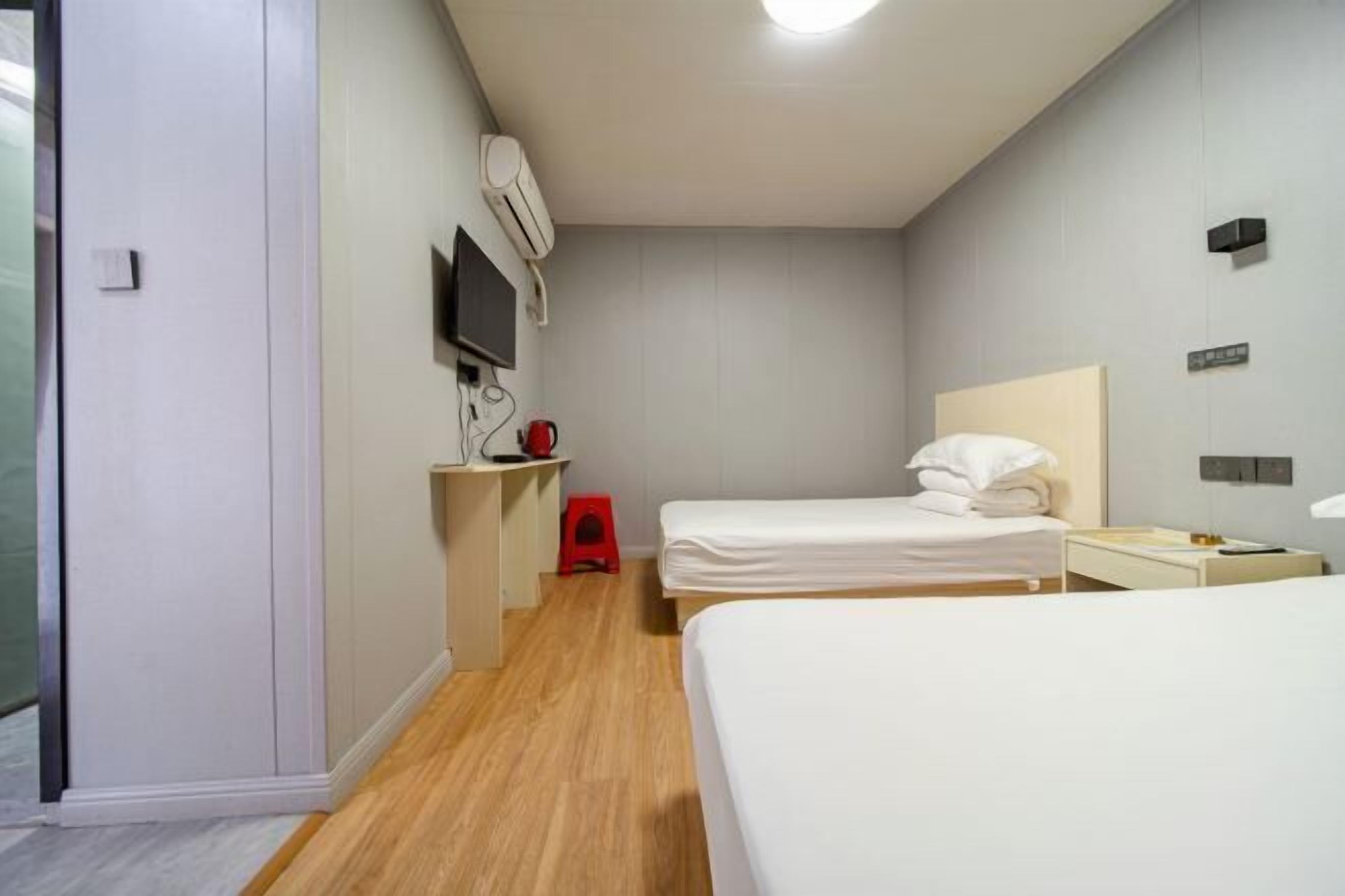 A hotel room with two beds, a desk, a TV, and a red stool.