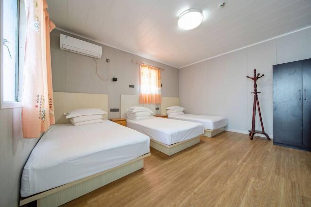 A room with three beds, a wardrobe, a window with curtains, and a standing lamp.