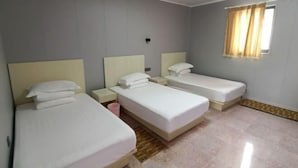 Habitación de hotel con tres camas individuales, una ventana pequeña con cortinas y suelo de baldosas.
