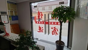 Un área de recepción con puerta de cristal, una planta en maceta y un tablón de anuncios.