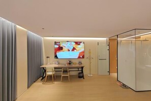 A modern room with a wooden floor, a desk with a chair, a large screen, and a glass partition. - Waltz Hotel (Huaibei)
