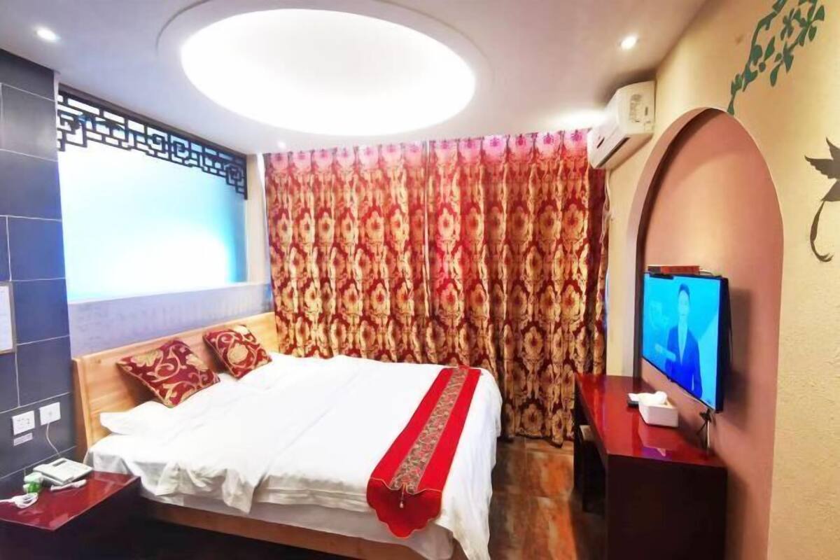 A hotel room with a bed, a TV, a nightstand, and a curtain.