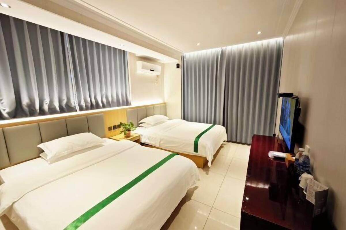 A hotel room with two beds, a desk, a TV, and a window with curtains.