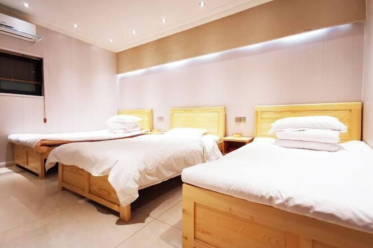 A hotel room with two wooden beds, a window, and an air conditioning unit.