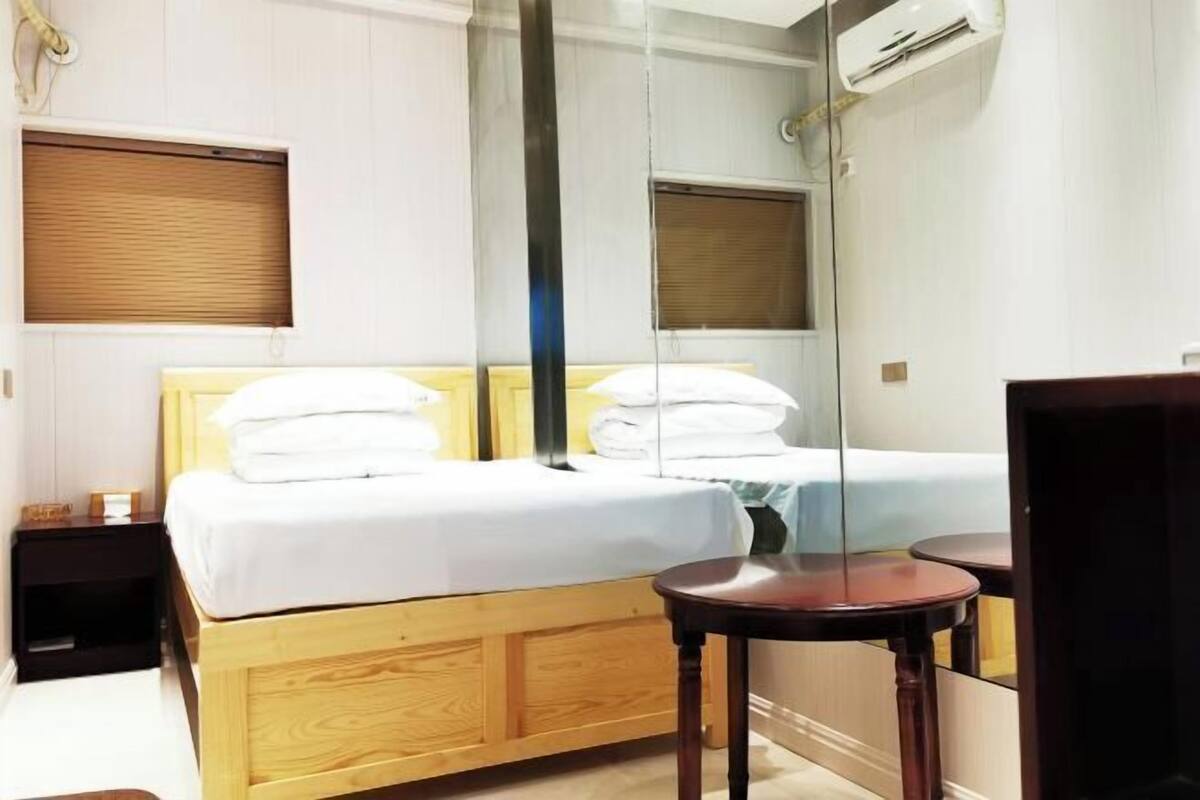 A bedroom with a wooden bed, a bedside table, a round table, and a mirror.