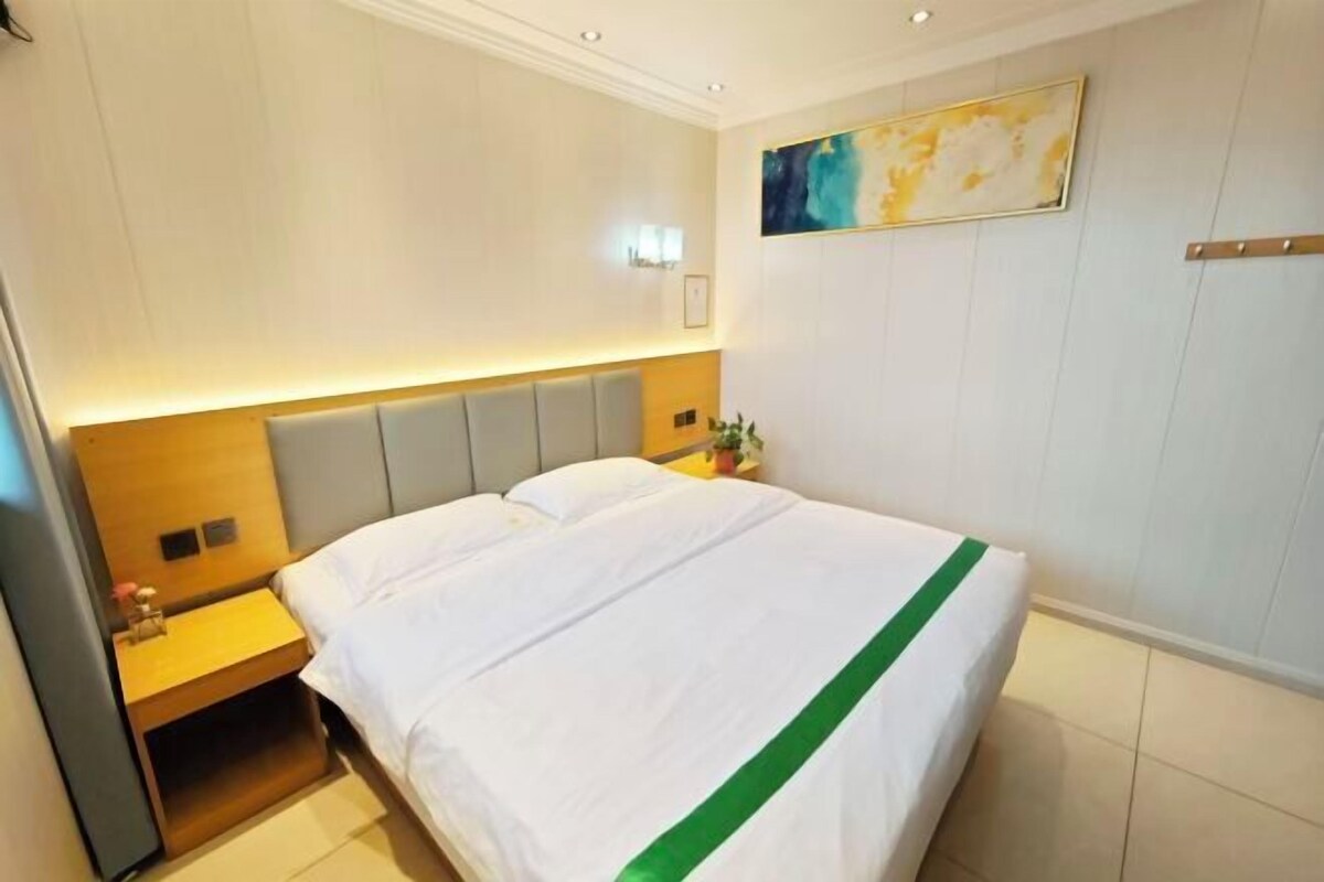 A hotel room with a bed, a nightstand, a wall-mounted light, and a painting.