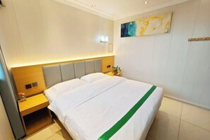 A hotel room with a bed, a nightstand, a wall-mounted light, and a painting. - Waltz Hotel (Huaibei)