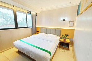 A hotel room with a bed, a nightstand, a wall-mounted lamp, and a window with curtains. - Waltz Hotel (Huaibei)