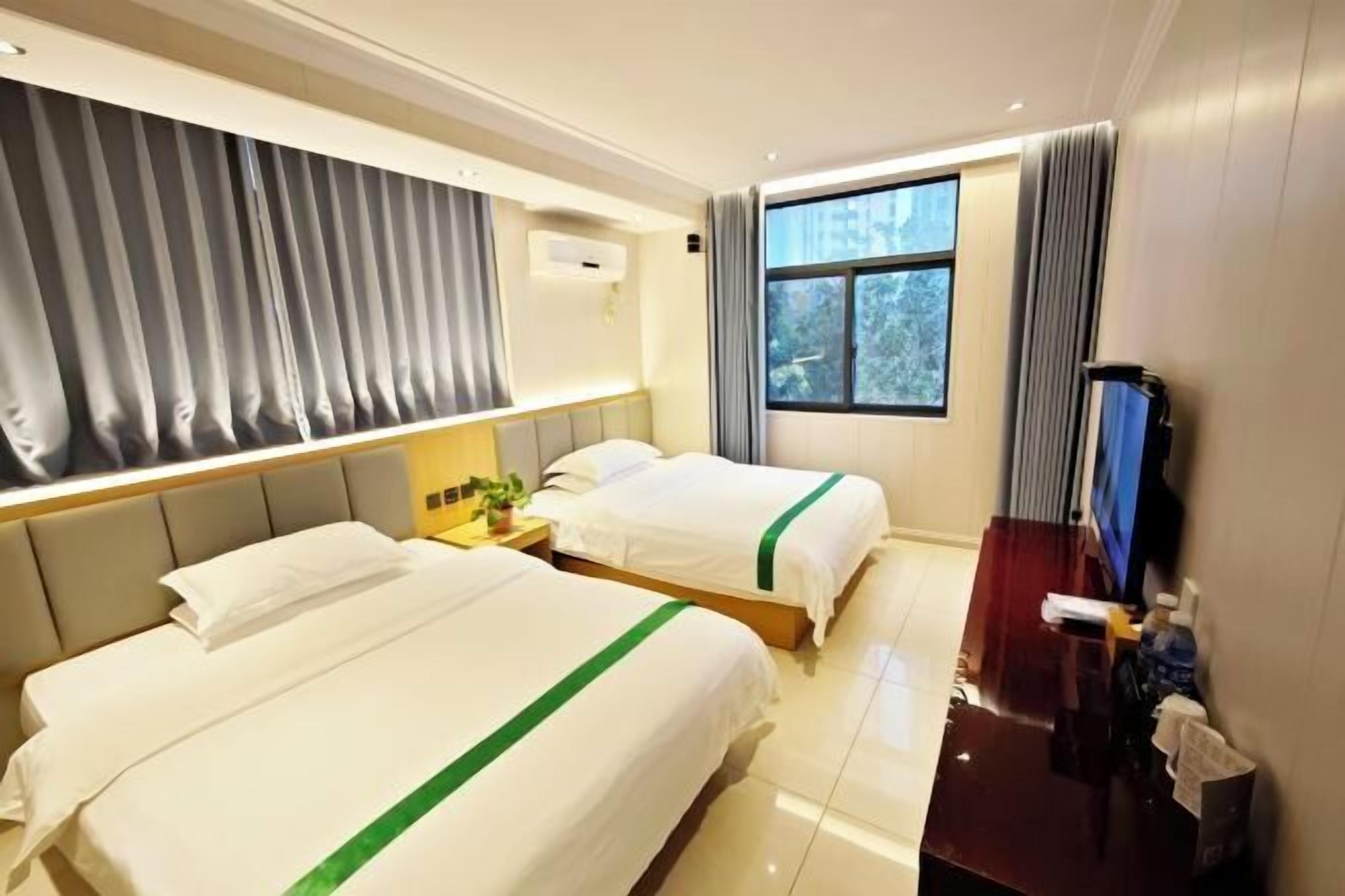 A hotel room with two beds, a TV, a desk, and a window with curtains.