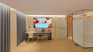 A modern room with a wooden floor, a desk with a chair, a large flat-screen TV, and a glass partition. - Waltz Hotel (Huaibei)