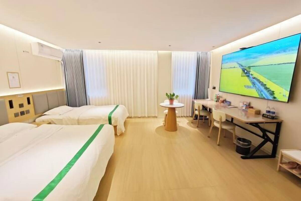 A hotel room with two beds, a desk, a TV, and a window with curtains.
