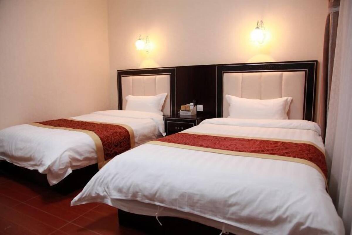 Two twin beds with headboards, a red bed runner, and wall-mounted light fixtures.