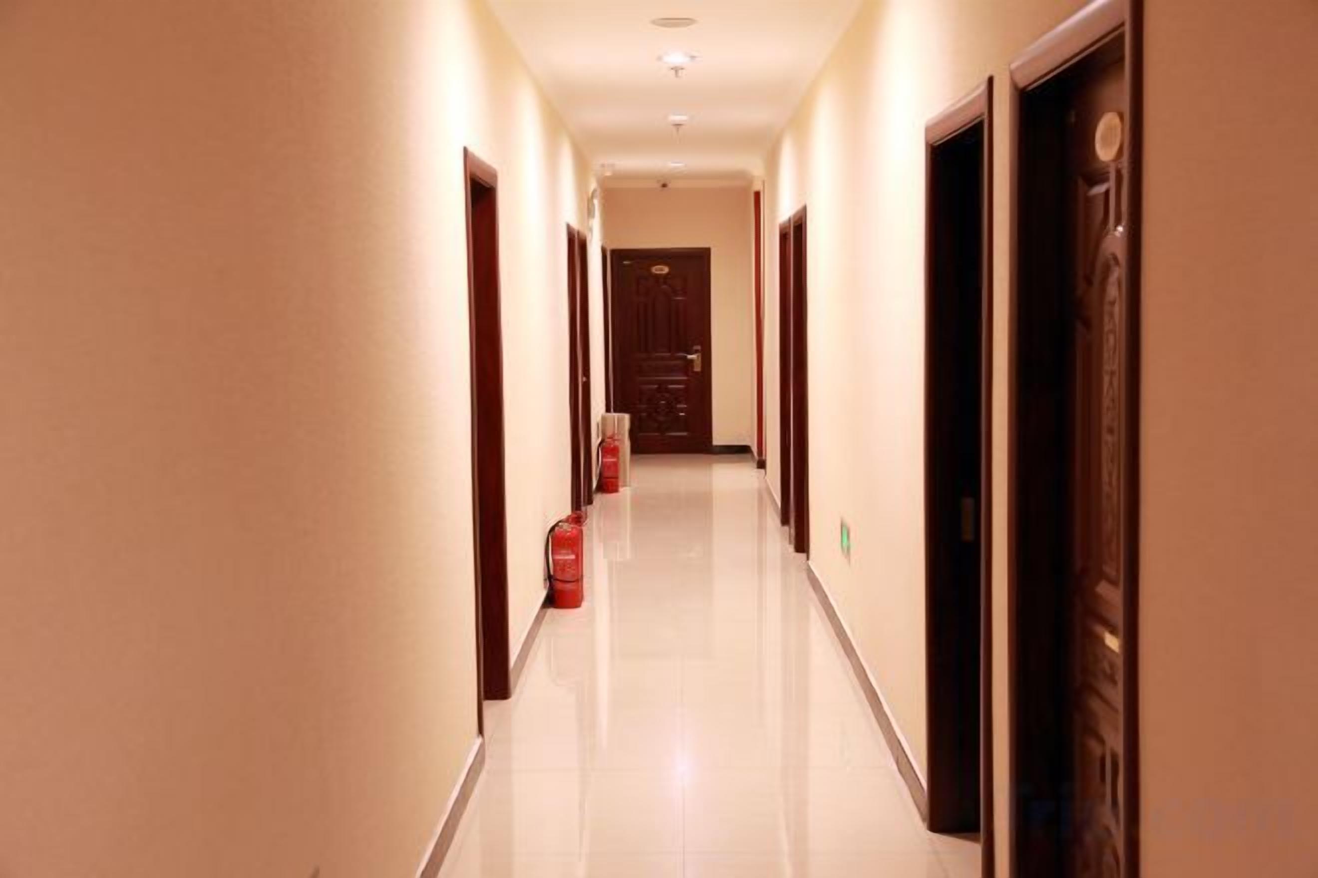 A hotel corridor with doors on both sides, a fire extinguisher, and a clean floor.