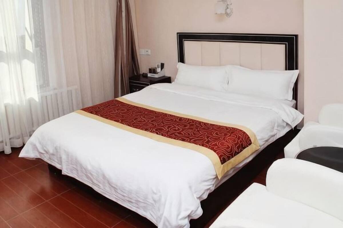 A neatly made bed with a white and red bedspread, a bedside table with a lamp, and a chair in a hotel room.