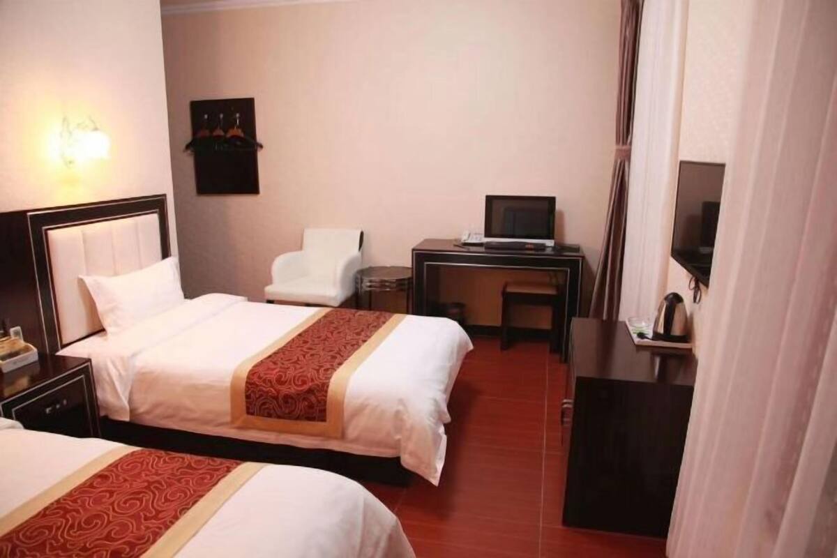 A hotel room with two beds, a desk with a computer, a chair, a TV, and a small cabinet.