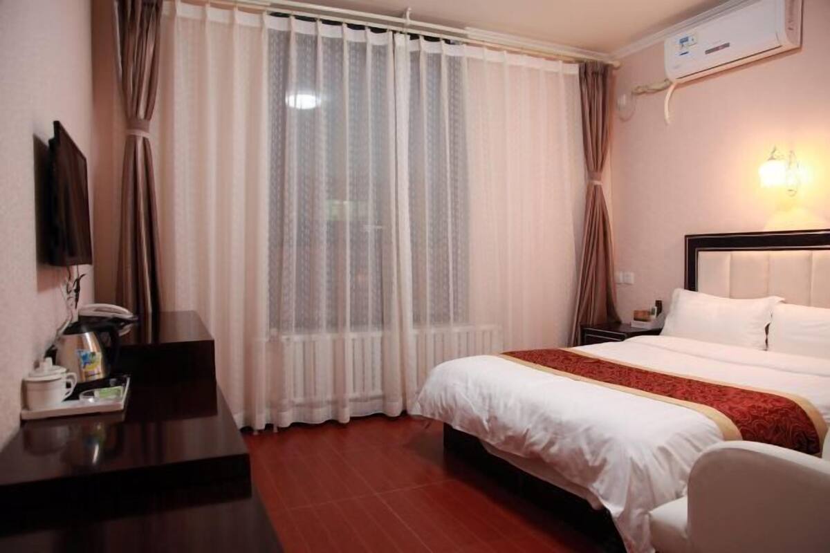 A hotel room with a bed, a desk with a telephone and a coffee maker, a TV mounted on the wall, and a window with curtains.