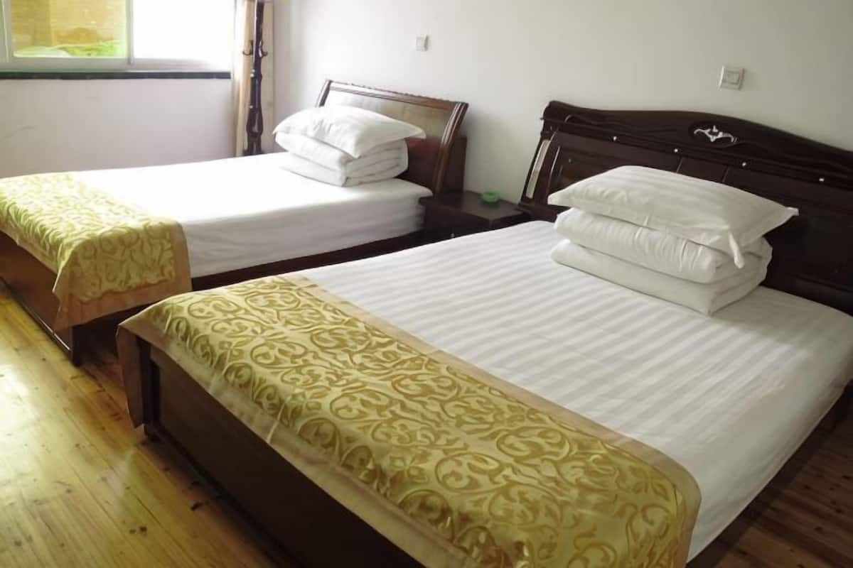Une chambre d’hôtel avec deux lits simples, un plancher en bois et une fenêtre avec des rideaux.