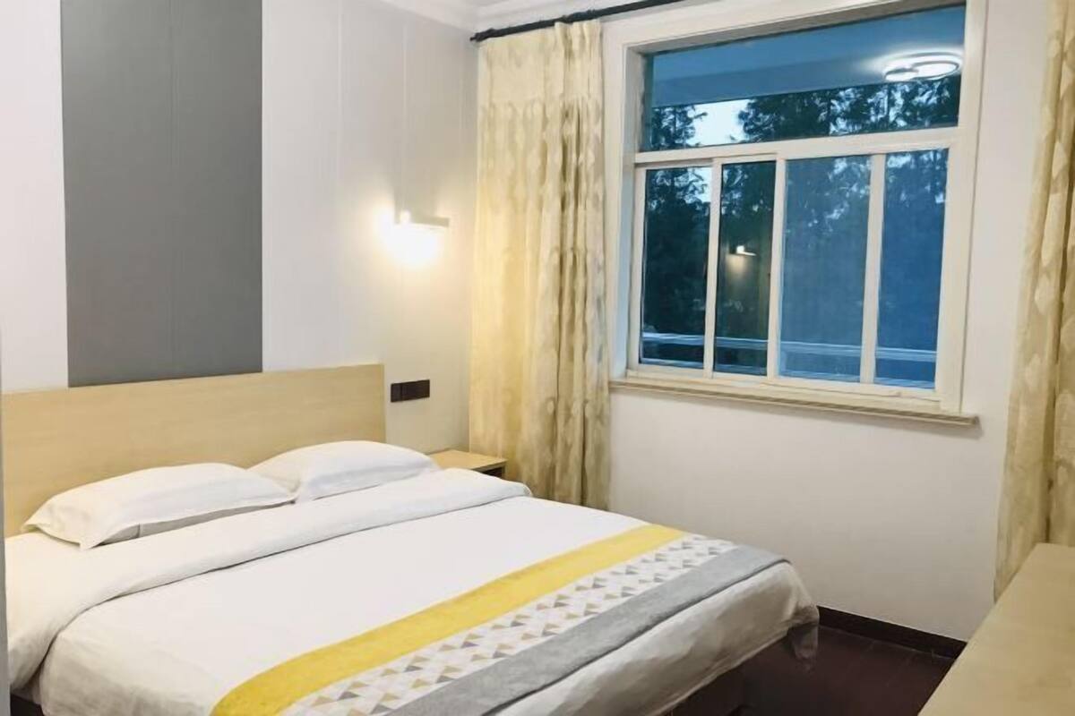 Une chambre d’hôtel avec un lit, une fenêtre avec des rideaux et une table de chevet.