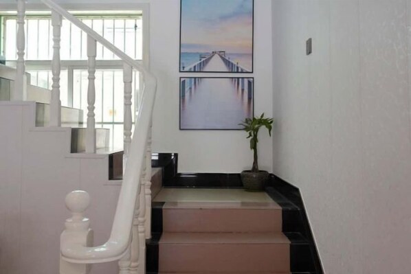 Una escalera con balaustres blancos y barandilla negra que conduce a un rellano con una planta en maceta y dos cuadros con imágenes de un muelle.