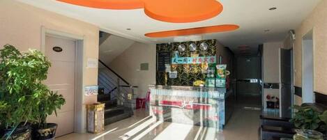 A hotel lobby with a reception desk, a staircase, and a potted plant.