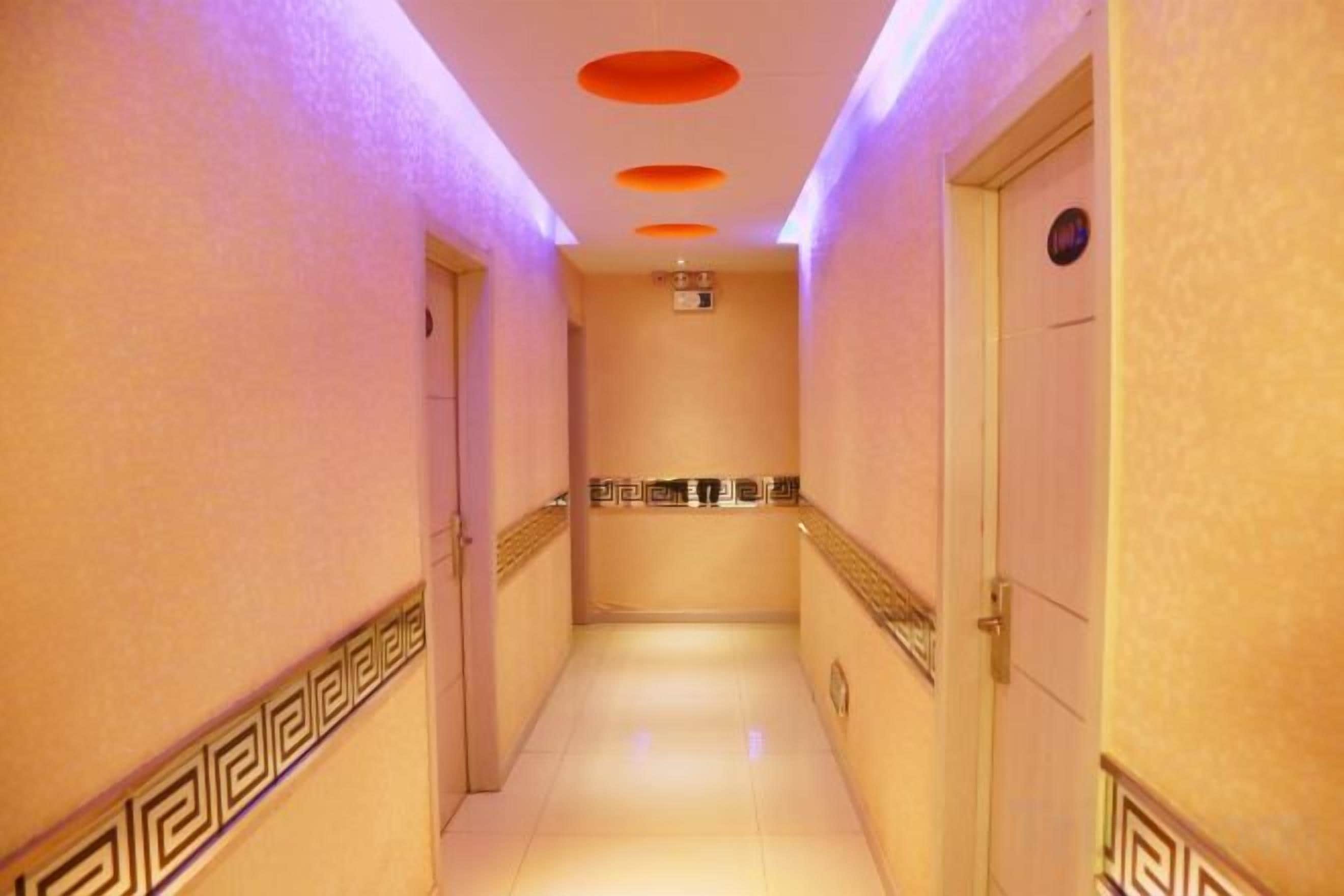 A hotel corridor with a tiled floor, a handrail on the right, and a door at the end.