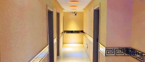 A hotel hallway with a reflective floor, decorative wall patterns, and a central light fixture.
